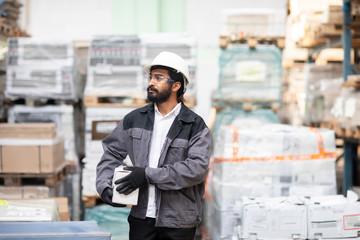Young man wearing hard hat working in a warehouse carrying a box