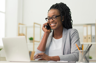 Black Young Lady Having Phone Conversation Sitting At Workplace