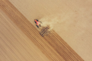 Tractor cultivates arable land with a disk harrow on an autumn day, view from a drone.
