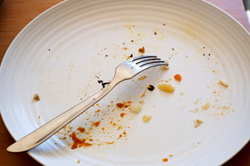 A white used plate with food crumbs and fork on table, fork is turned over.
