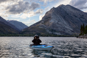 Adventurous Man Kayaking in Glacier Lake surrounded by the beautiful Canadian Rocky Mountains during a cloudy summer sunset. Taken in Upper Waterton Lake, Alberta, Canada.
