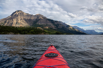 Kayaking in Glacier Lake surrounded by the beautiful Canadian Rocky Mountains during a cloudy summer sunset. Taken in Upper Waterton Lake, Alberta, Canada.