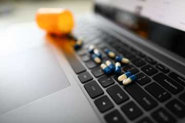 Yellow-blue pill capsules are scattered on black laptop keyboard. Reception of drugs at workplace concept.
