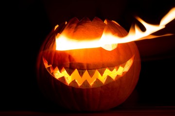 Fototapeta premium Spooky carved halloween pumpkin with glowing hot fire flame eyes. Big helloween autumn symbol with mad face, glowing eyes, mouth and teeth. Scary hot nightmare horror with evil smile at october 31st