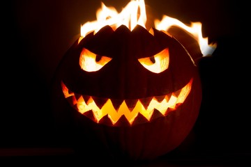 Carved spooky halloween pumpkin with glowing hot fire flame head. Big helloween autumn symbol with mad face, glowing eyes, mouth and teeth. Scary hot nightmare horror with evil smile at october 31st