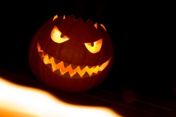 Spooky carved halloween pumpkin in hot burning hell fire flames. Big helloween autumn symbol with mad face, glowing eyes, mouth and teeth. Scary hot nightmare horror with evil smile at october 31st