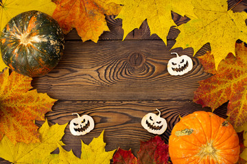 Halloween background with pumpkins, autumn leaves and creepy pumpkins carved from wood. Flat lay