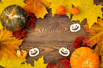 Halloween background with pumpkins, autumn leaves and creepy pumpkins carved from wood. Flat lay