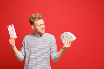 Portrait of happy young man with money fan and lottery ticket on red background