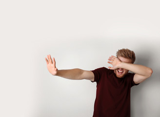 Young man being blinded and covering eyes with hand on light background