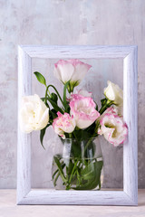 Eustoma flowers in vase in photo frame on table near stone wall, space for text. Blank for postcards
