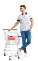 Young man with empty shopping cart on white background