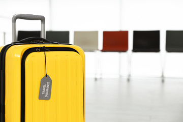 Yellow suitcase with label indoors, space for text. Travel insurance