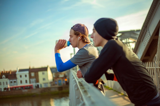 Two young men drinking water after a run by River Thames, London, UK