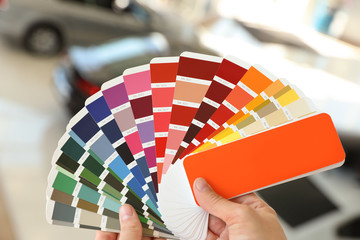 Young woman holding palette with color samples at car service station, closeup