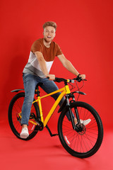 Handsome young man riding bicycle on red background