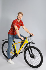 Handsome young man riding bicycle on grey background