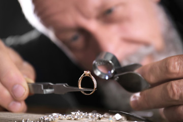 Male jeweler evaluating diamond ring in workshop, closeup view