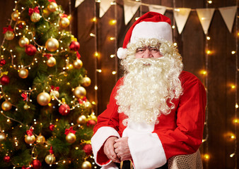 Fototapeta na wymiar Santa Claus portrait, sitting indoor near decorated xmas tree with lights - Merry Christmas and Happy Holidays!