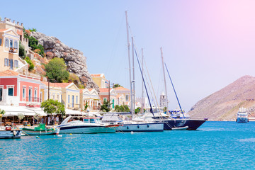 Wonderful view on colorful houses on rocks and sailing boats on dock of deep blue Mediterranian sea on Greek island Symi on sunbeams, holidays on exotic islands
