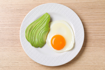 Plate of fried egg and avocado on wooden table, top view. Healthy breakfast