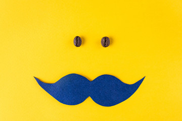 Movember concept. Blue paper mustache and grains of coffee on a bright yellow background....