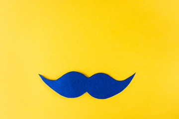 Movember concept. Blue paper mustache on a bright yellow background. Contrasting colors, minimalism, flat lay, top view. The fight against prostate cancer, male diseases.