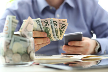 Male hand holding pack of banknotes and cellphone making some calculation planning his future...