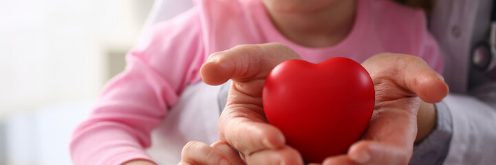 Little baby girl visiting doctor holding in hands red toy heart as life safe symbol