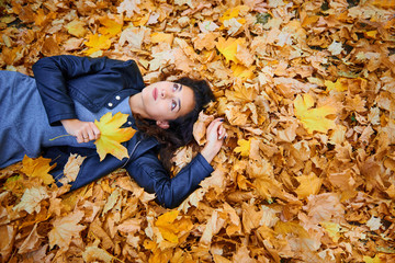 woman lying with autumn leaves in city park, outdoor portrait