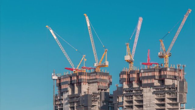 Aerial view of a skyscrapers under construction with huge cranes timelapse in Dubai marina. Blue sky on a background. United Arab Emirates