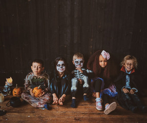 Group of pretty kids in Halloween costumes are sitting on the floor near candles.