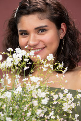 girl with curly hair holding flowers smiling and looking at the camera- Hispanic woman in studio - natural young woman