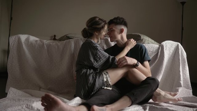 Young beautiful lovely couple is having a romantic time. Sitting on the floor by the bed embracing and smiling