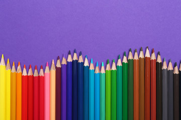 Colorful pencils on purple background, flat lay. Space for text