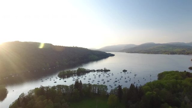 4K aerial of sunset over Scottish lake in the Highlands. Blue still waters with sailing boats and woodland in a British summer tourist nature landscape in Scotland.