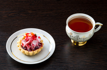 Basket-cake with jam on the plate and tea cup on dark background