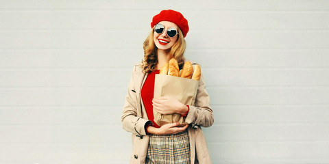 Portrait beautiful smiling woman holding grocery shopping paper bag with long white bread baguette...