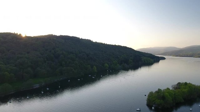 4K aerial of sunrise over Scottish lake in the Highlands. Blue still waters with sailing boats and woodland in a British summer tourist nature landscape in Scotland.