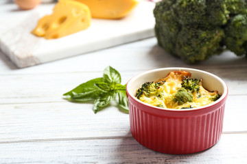 Tasty broccoli casserole in ramekin on white wooden table