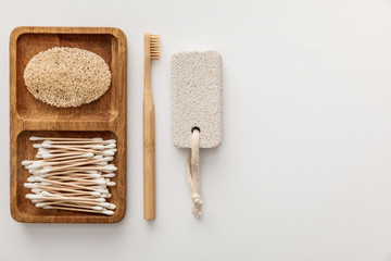 Fototapeta na wymiar flat lay with wooden dish with cotton swabs and loofah near toothbrush and pumice stone on white background