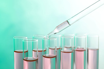 Dropping sample into test tube with liquid on color background, closeup