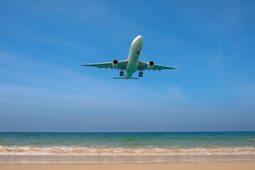 Fototapeta na wymiar Passenger Airplane flies over a beautiful beach with fine sand and blue sea.