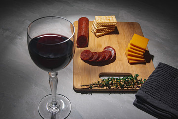 Sliced pepperoni on a bamboo cutting board with  cheddar cheese and crackers on a marble table.