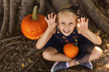 Adorable Young Child Girl Enjoying the Pumpkins. Girl Ready for outdoor Halloween Party. Big Old Wood on a Background. Halloween Concept...