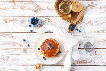 Plate with tasty pancakes, blueberries and honey on white table