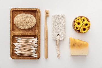 flat lay with wooden dish with cotton swabs and loofah near toothbrush, piece of soap, pumice stone...