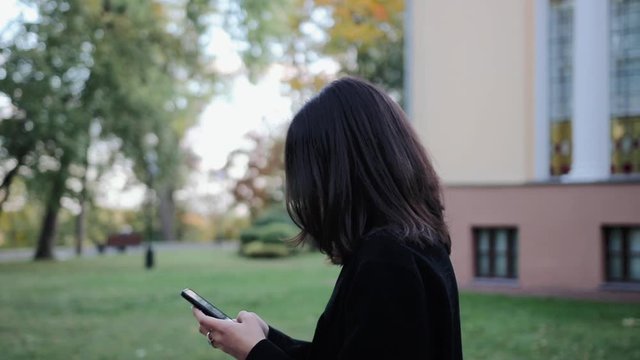 young woman using her smartphone and texting a message while chatting in social media in the park