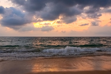 Obraz premium Beautiful sunset seascape. Sunlight is visible in the cloudy sky. Below is a stormy sea and a sandy wet shore.