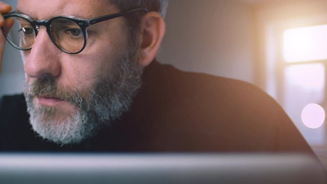 Businessman with glasses working on laptop computer in his office, thinking, reading and analyzing data media content